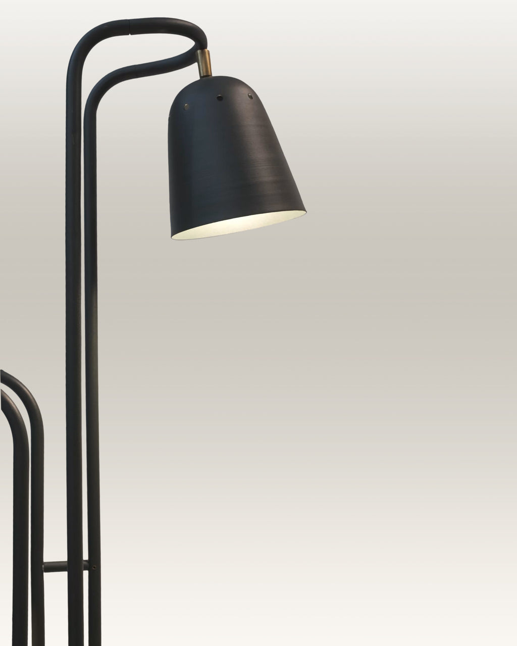 A modern black dual-arm floor lamp stands beside a tan leather sofa in a sunlit living room 