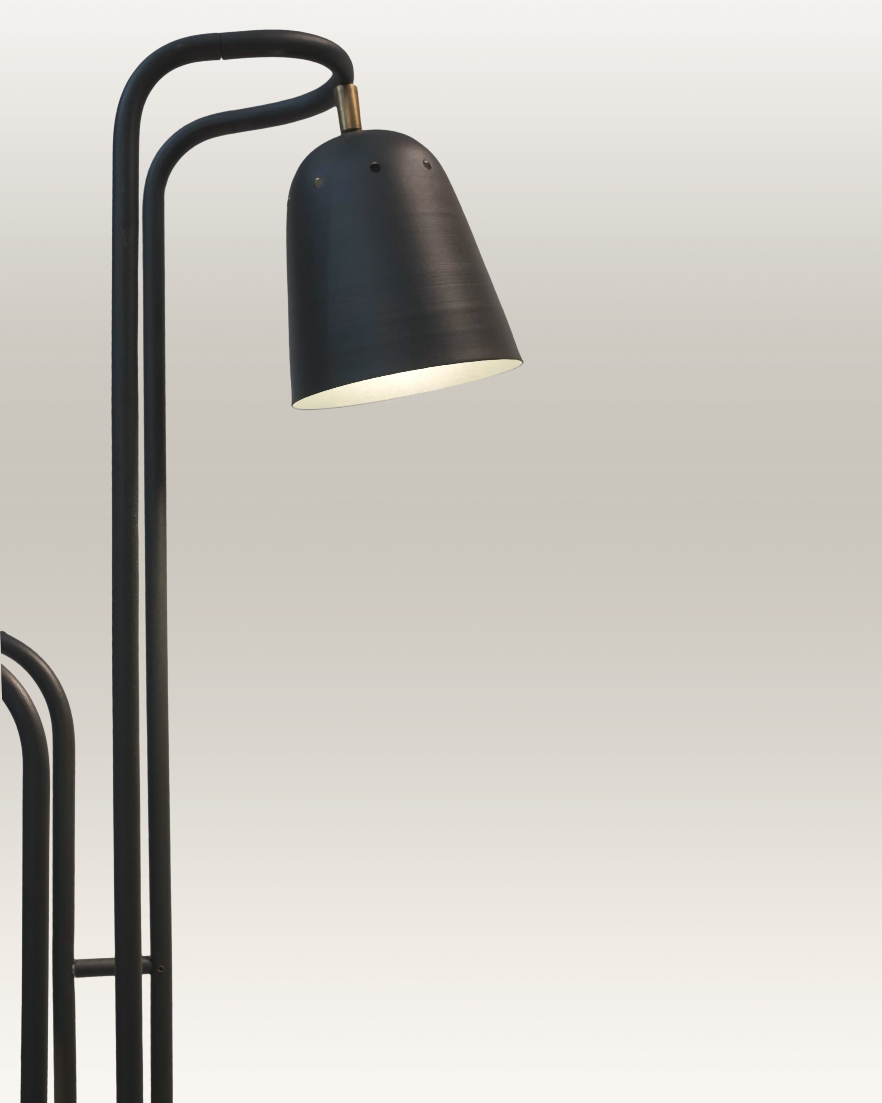 A modern black dual-arm floor lamp stands beside a tan leather sofa in a sunlit living room 