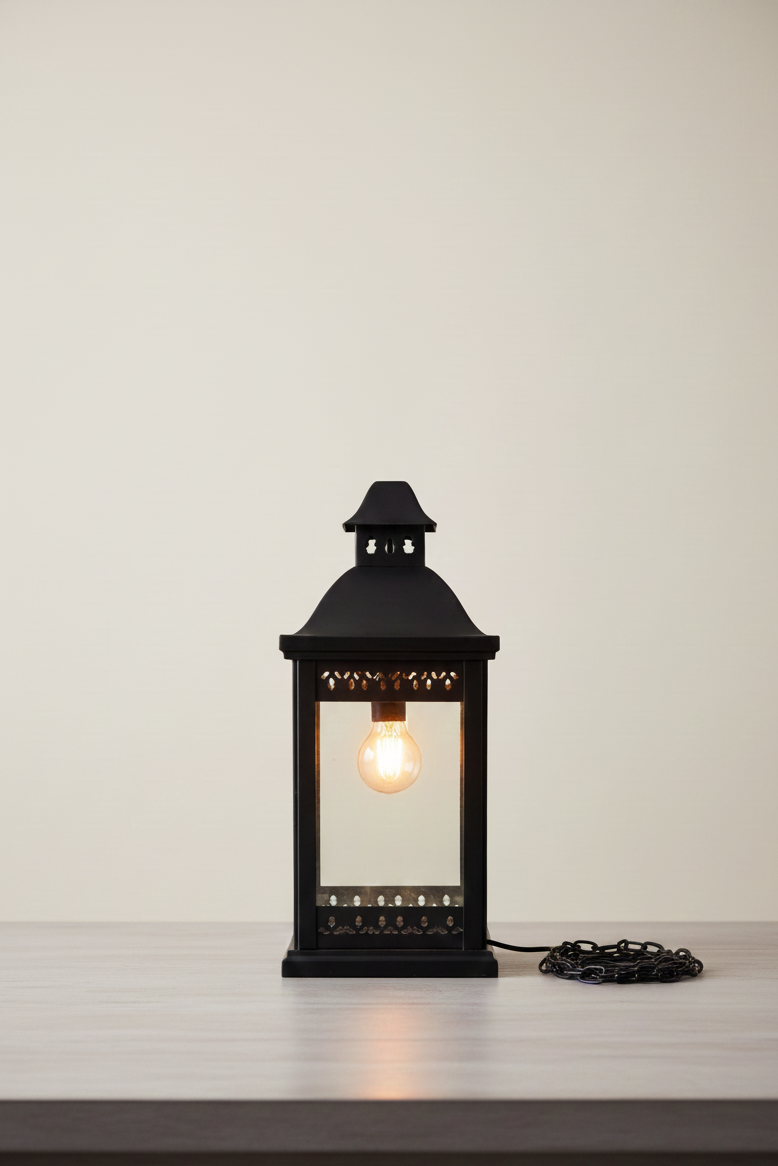 Black lantern-style table lamp with a lit bulb on a white surface and light gray background