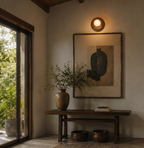 Handcrafted solid wood wall sconce featuring an 8-inch natural wooden backplate with a centered 4-inch frosted opal glass globe, photographed in soft daylight against a textured plaster wall in a warm mid-century modern interior.