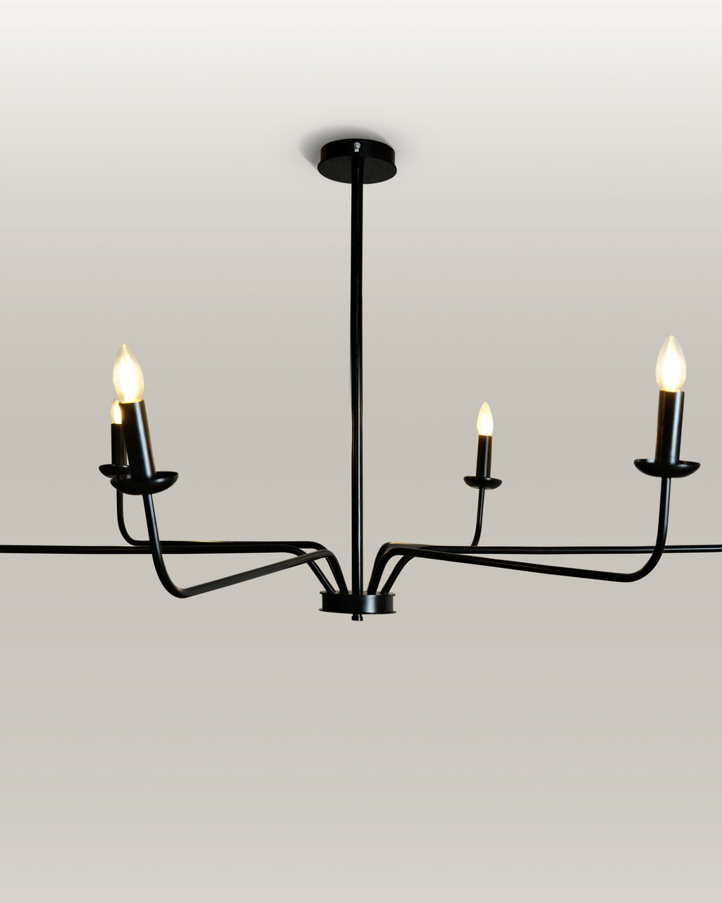 Minimalist chandelier featuring six black metal arms and candle flame light bulbs, illuminating a contemporary dining area.