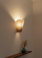 Wall-mounted lamp with checkered shade casting light on a plain wall.