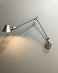 Wall-mounted lamp with two adjustable arms on a plain wall.