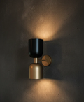 Wall-mounted light fixture with black and gold design on a dark wall.