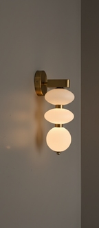 Wall-mounted light fixture with three round glass shades on a plain wall.
