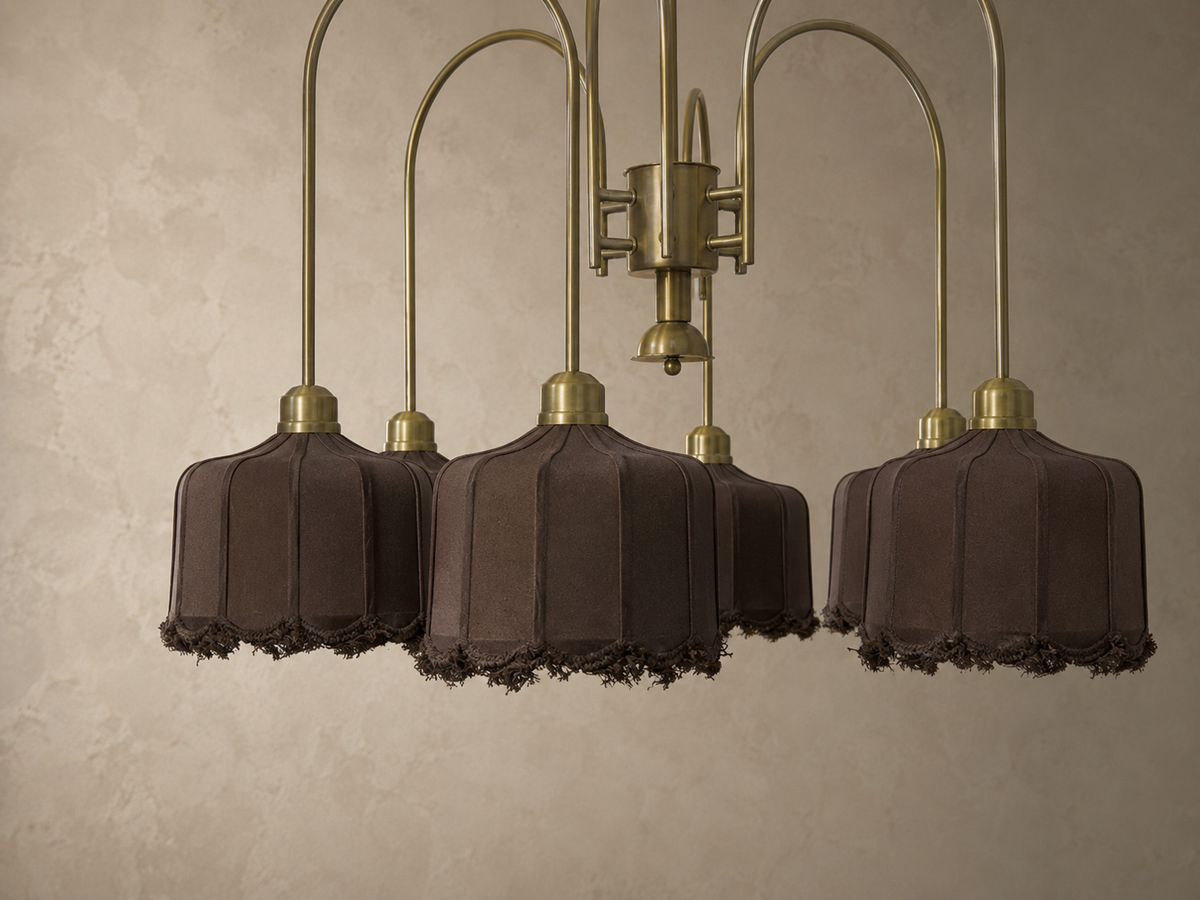 A multi-light chandelier with five dark brown fabric bell shades and fringed edges, suspended from curved brass-toned metal arms against a textured beige wall.