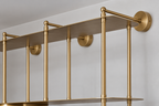 Gold metal wall-mounted shelving with vertical support rods and two horizontal shelves, shown installed against a white wall.